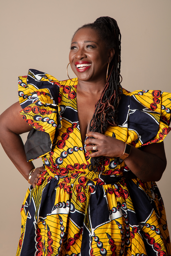 Abena Koomson Headshot, photo of Abena Koomson smiling with vibrant yellow black and red dress