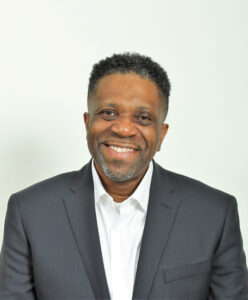 David Stamps is seen chest up looking at the camera with a gentle smile wearing a sports jacket over a white dress shirt